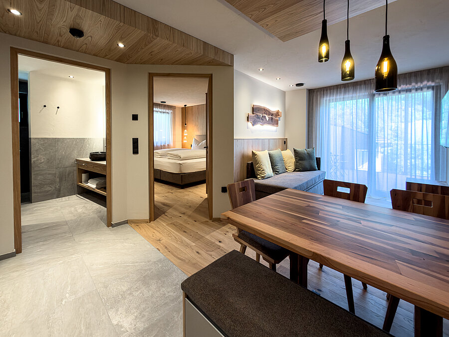 Offener Wohnbereich im Bio-Wein-Apartment – Weingut Santer Blick vom offenen Essbereich mit Massivholztisch auf das Sofa, das angrenzende Schlafzimmer und das Badezimmer im Weingut Santer.