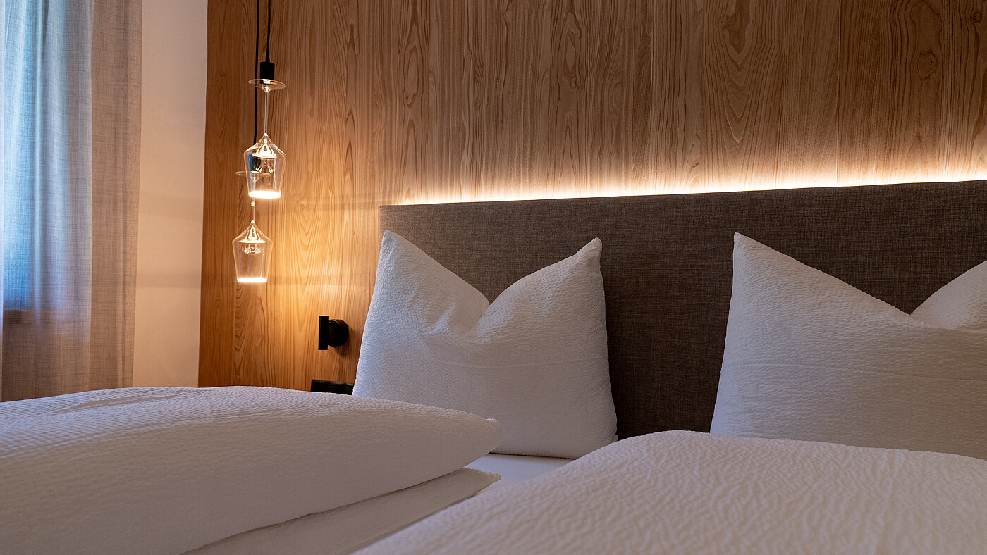 Modernes Schlafzimmer | Weingut Santer Südtirol Modernes Schlafzimmer mit hellem Holzboden, einer Holzwand, großem Einbauschrank und einem Doppelbett mit Kopfteil.