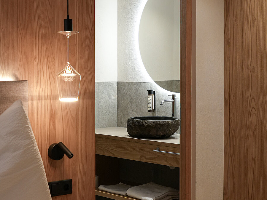 Modernes Badezimmer im Wein-Apartment – Bio-Weingut Santer Modernes Badezimmer mit Natursteinwaschbecken und beleuchtetem Spiegel, gesehen vom Schlafbereich aus im Weingut Santer.