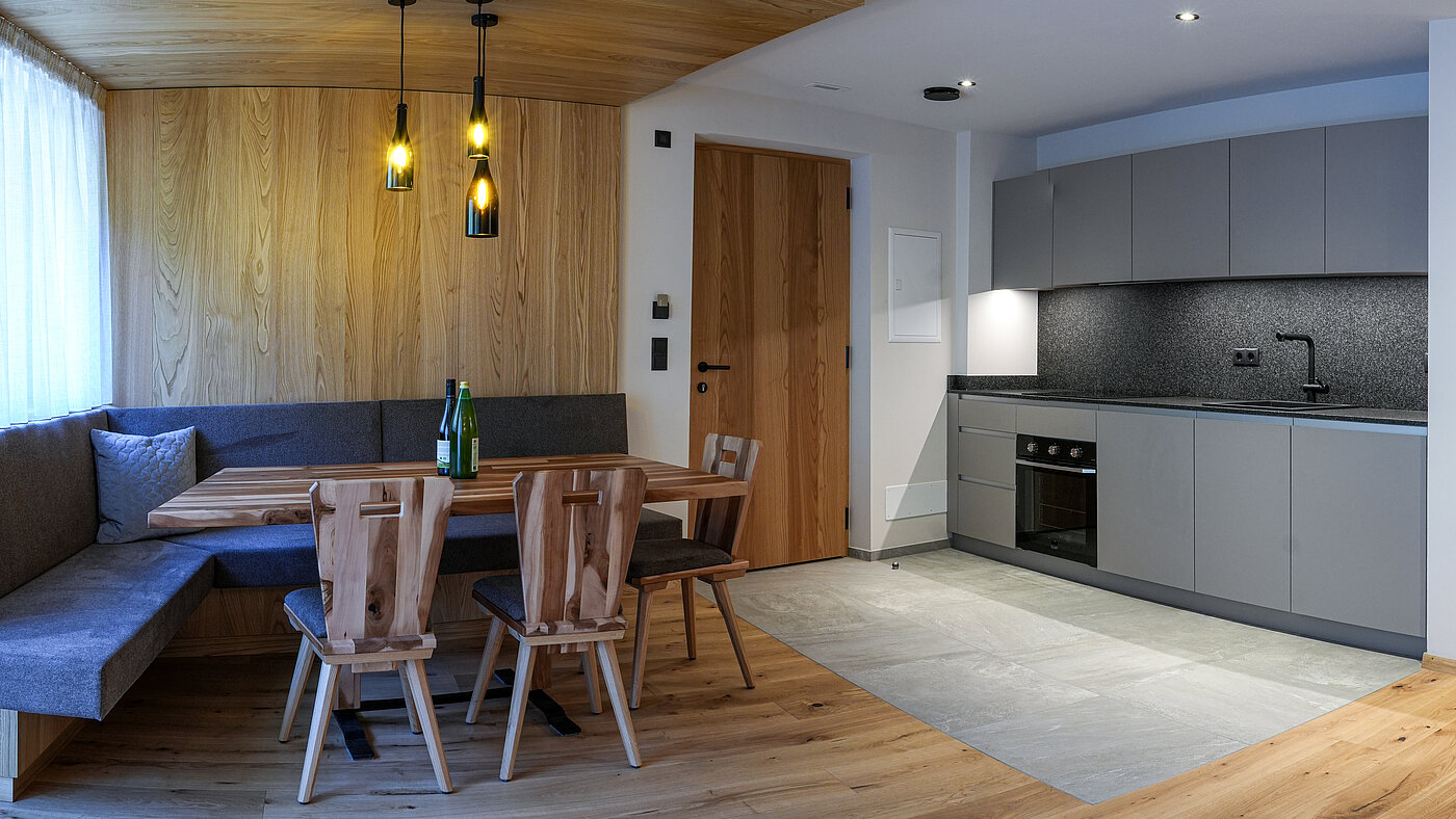 Moderne Wohnküche im Wein-Apartment – Bio-Weingut Santer Moderne graue Küchenzeile und gemütliche Holzecke mit einzigartigen Hängeleuchten aus Weinflaschen im Weingut Santer.