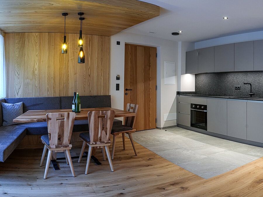 Moderne Wohnküche im Wein-Apartment – Bio-Weingut Santer Moderne graue Küchenzeile und gemütliche Holzecke mit einzigartigen Hängeleuchten aus Weinflaschen im Weingut Santer.