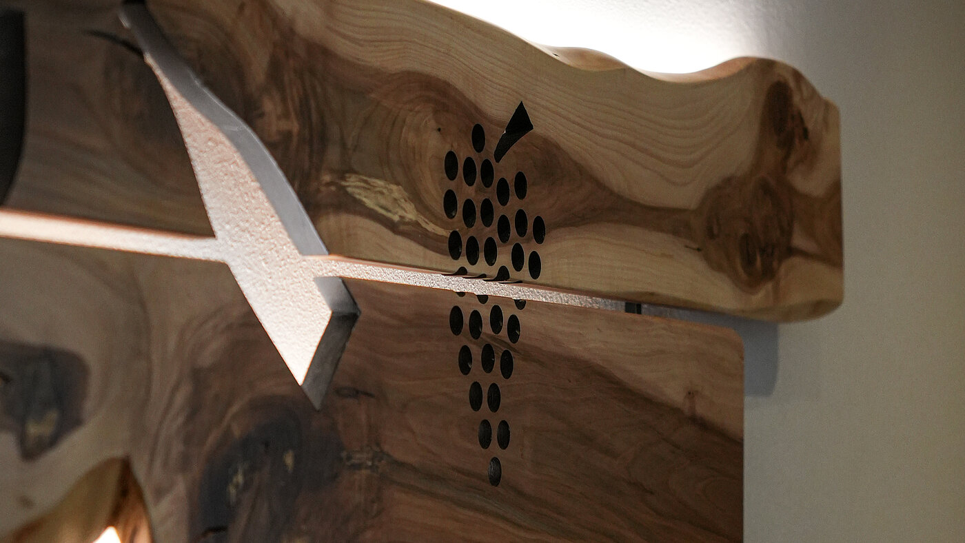 Wanddeko aus Holz mit Logo – Bio-Weingut Santer Südtirol Nahaufnahme einer beleuchteten Wanddekoration aus Naturholz mit dem eingravierten Logo des Weinguts Santer.