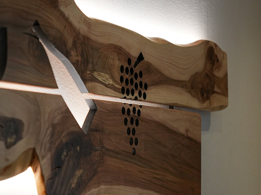 Wanddeko aus Holz mit Logo – Bio-Weingut Santer Südtirol Nahaufnahme einer beleuchteten Wanddekoration aus Naturholz mit dem eingravierten Logo des Weinguts Santer.