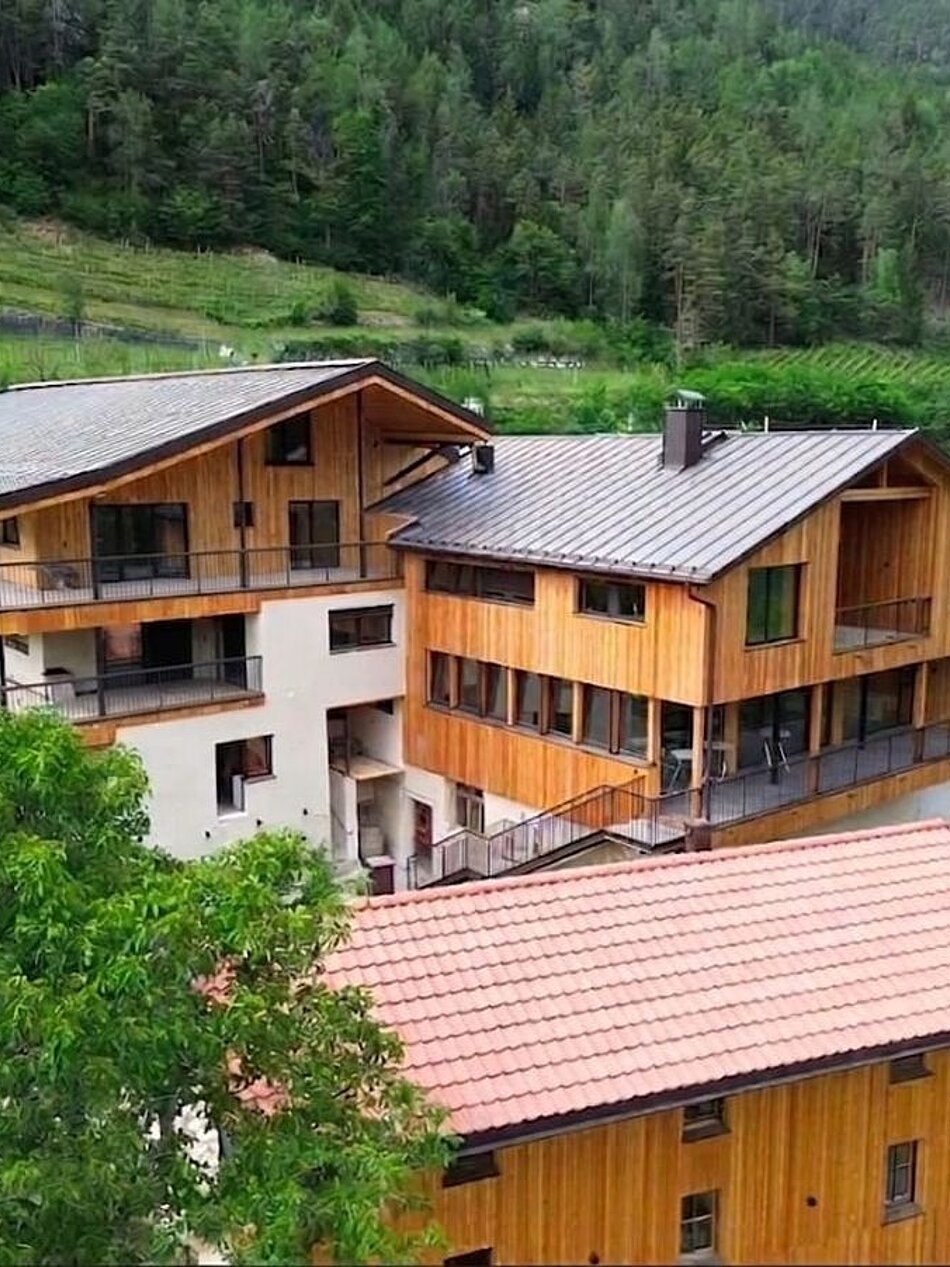 Bio-Weingut Santer mit Holzgebäuden inmitten von Weinbergen in Mühlbach, Südtirol, umgeben von grüner Natur.