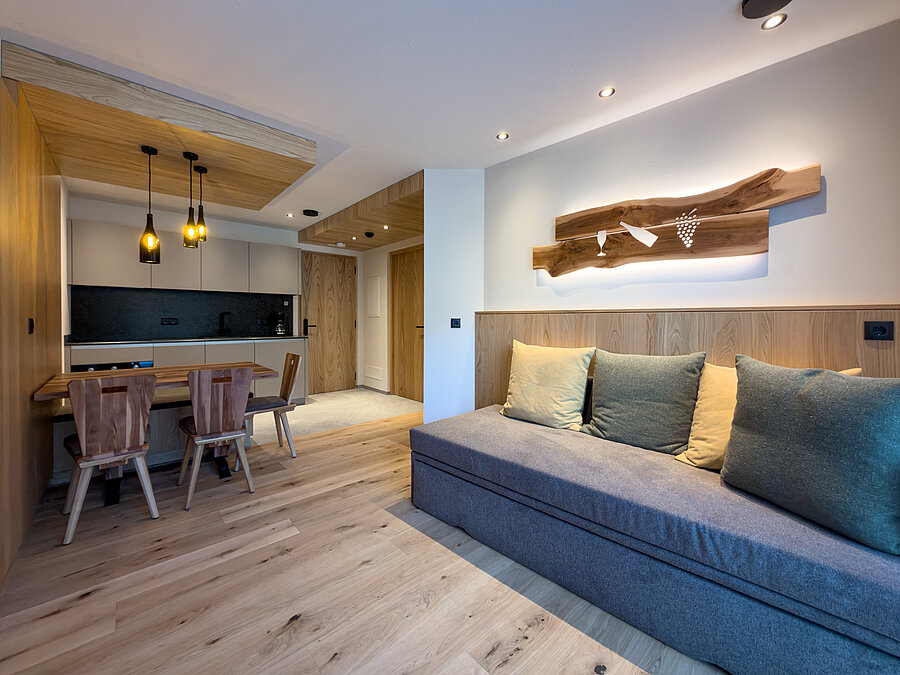 Gemütliche Sofaecke im Wein-Apartment – Bio-Weingut Santer Gemütliche graue Sofaecke mit Kissen und einer beleuchteten Holzkunst-Wanddekoration im Apartment des Weinguts Santer.