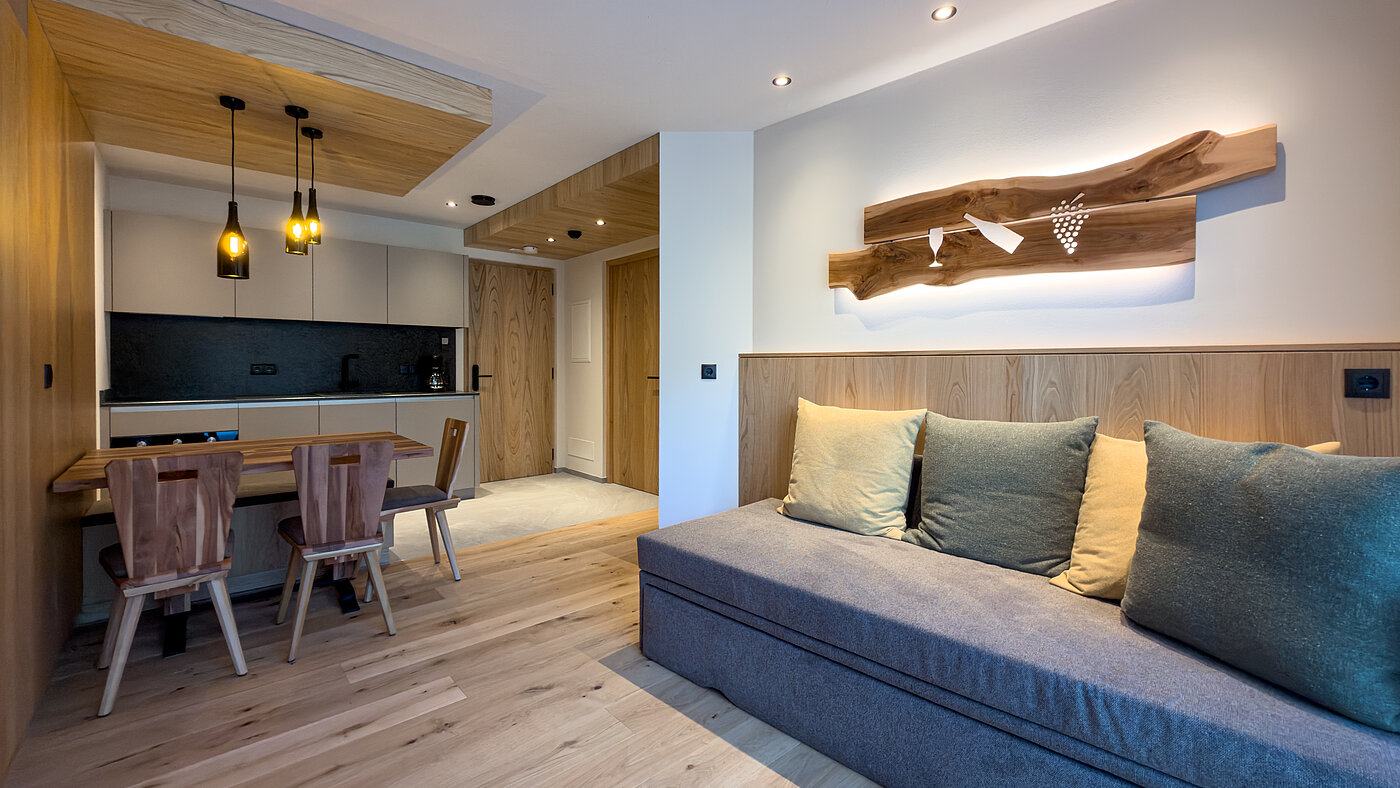 Gemütliche Sofaecke im Wein-Apartment – Bio-Weingut Santer Gemütliche graue Sofaecke mit Kissen und einer beleuchteten Holzkunst-Wanddekoration im Apartment des Weinguts Santer.