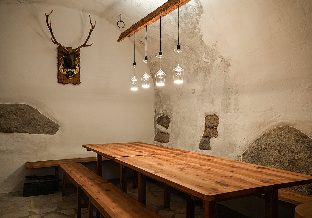Weinkeller im Bio-Weingut Santer in Mühlbach Südtirol Rustikaler Weinkeller mit Holztisch, Bänken und moderner Beleuchtung im Bio-Weingut Santer in Mühlbach Südtirol.