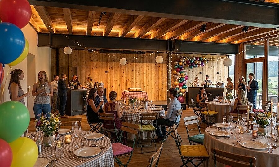 Private Feiern & Feste in Südtirol | Weingut Santer Festlich dekorierter Innenraum einer modernen Eventlocation mit Holzwänden, Luftballons, Lichterketten und Gästen an gedeckten Tischen bei einer Feier.