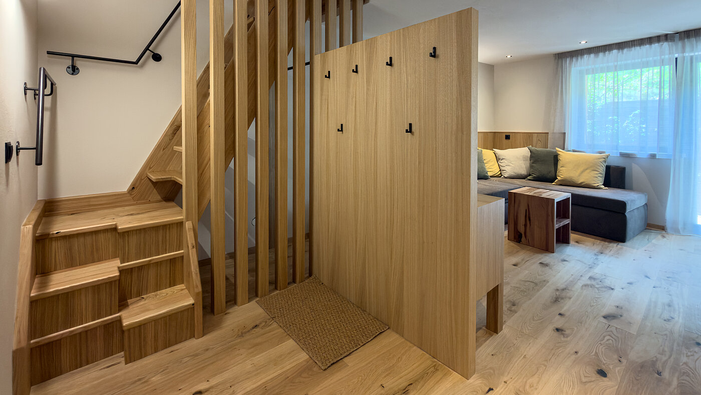Eingangsbereich mit Holztreppe im Wein-Apartment – Weingut Santer Eingangsbereich einer Ferienwohnung im Weingut Santer mit moderner Massivholztreppe, hölzernem Raumteiler und Blick auf das Sofa.