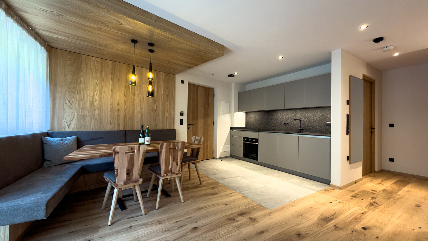 Wohnküche mit gemütlicher Essecke – Bio-Weingut Santer Offene, moderne Wohnküche mit grauer Küchenzeile, Holzboden und einer großen gemütlichen Eckbank-Essecke im Weingut Santer.