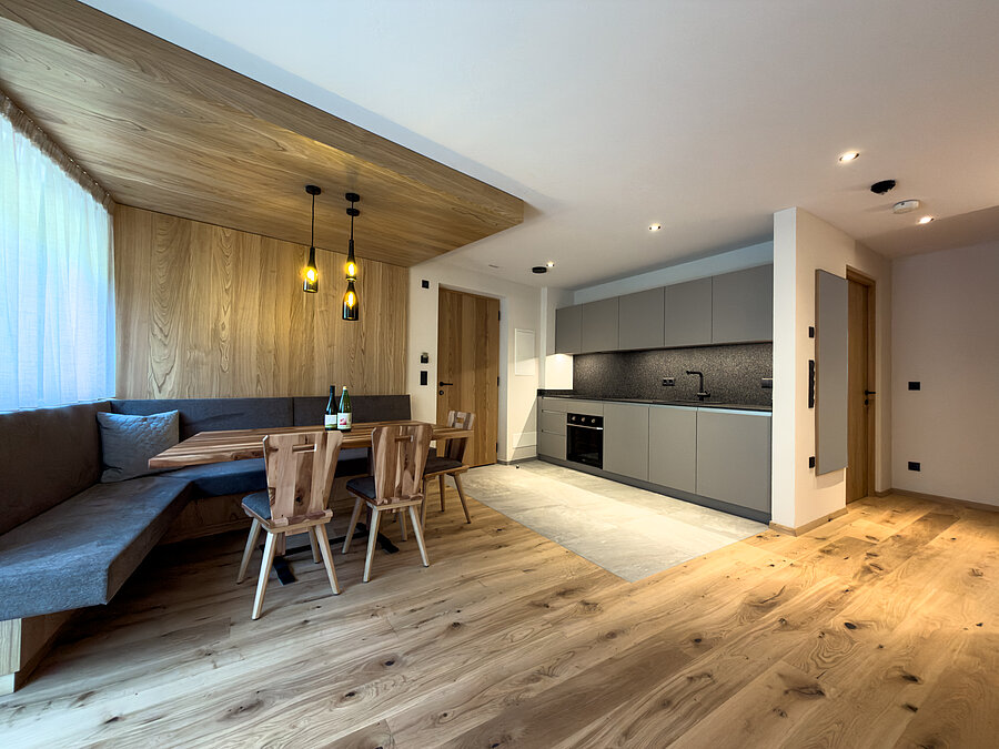 Wohnküche mit gemütlicher Essecke – Bio-Weingut Santer Offene, moderne Wohnküche mit grauer Küchenzeile, Holzboden und einer großen gemütlichen Eckbank-Essecke im Weingut Santer.